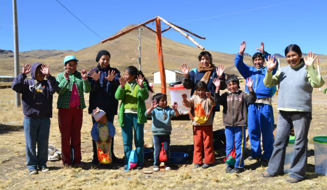 Grupo de madres, niñas y niños altoandinos participando en actividad comunitaria al aire libre con enfoque de salud y bienestar.